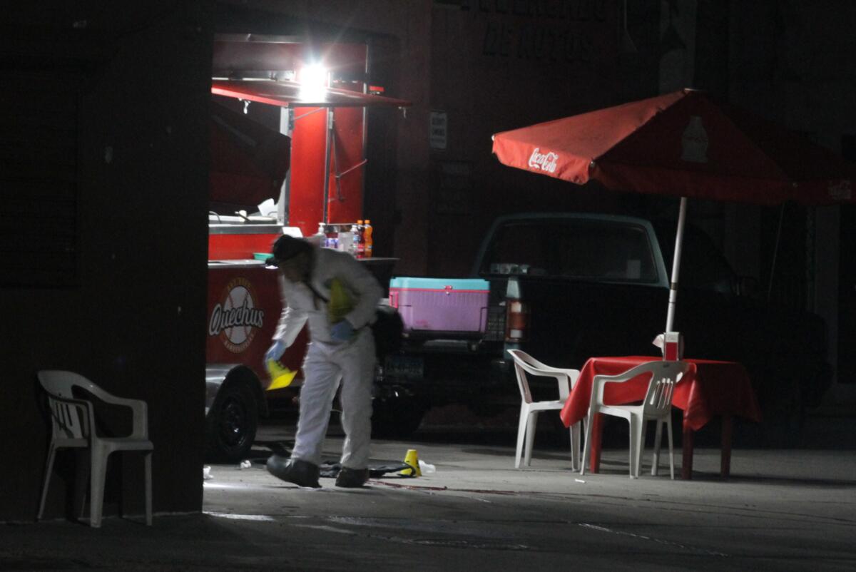 A forensics team member investigates the hot dog stand where a group of state police officers were ambushed in Tijuana's Benton neighborhood shortly before midnight Wednesday. One officer was killed.