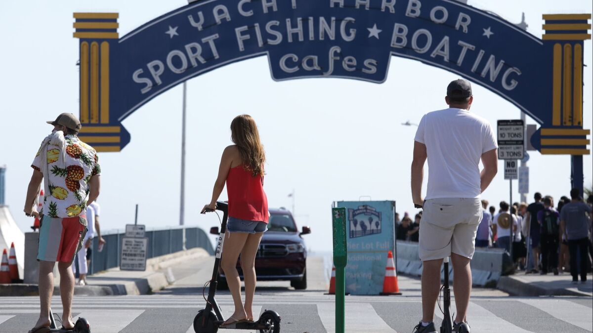 Scooter riders roll past the sign for the Santa Monica Pier.