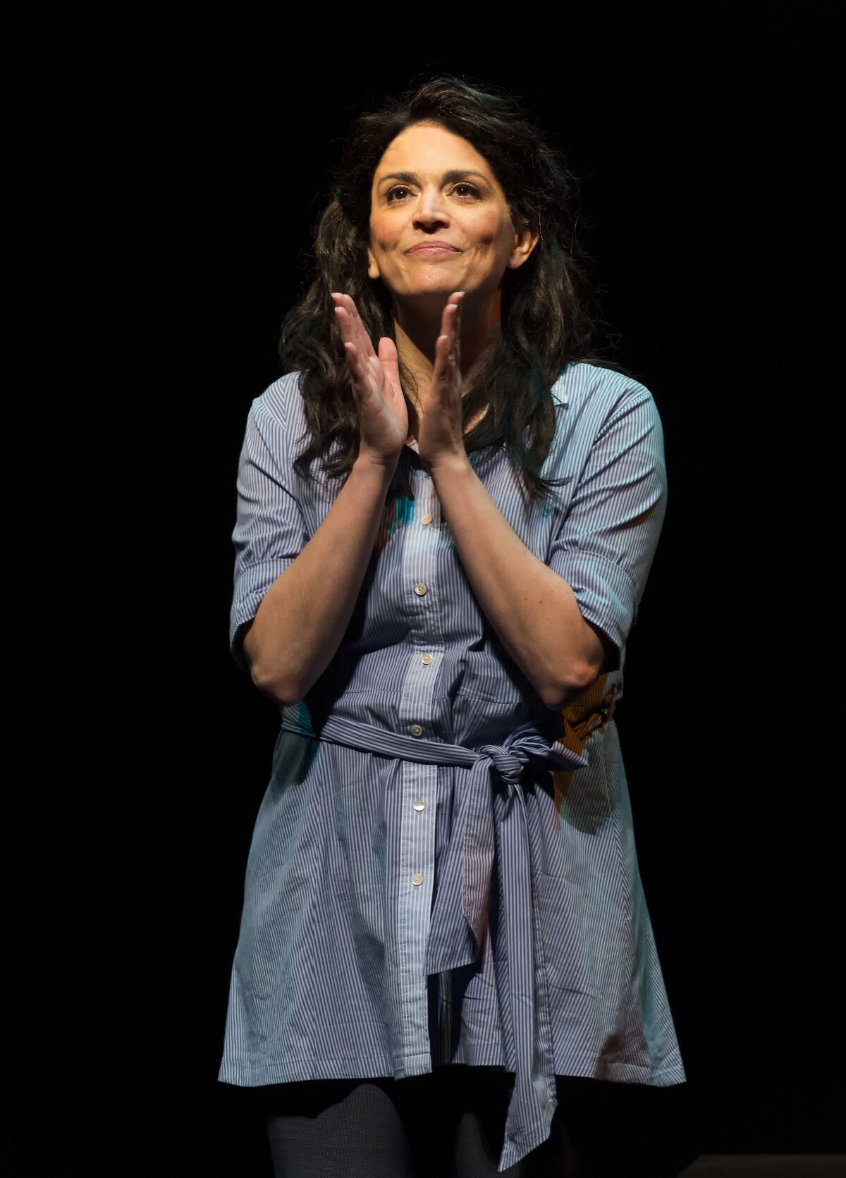 A woman on stage with her hands together.