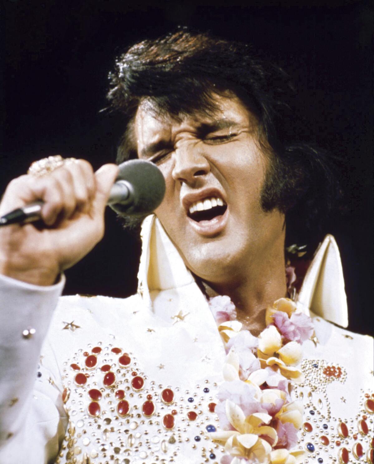 A man in a spangly outfit sings into a microphone.