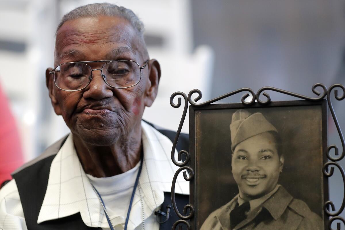 FILE - In this Sept. 12, 2019 file photo, World War II veteran Lawrence Brooks holds a photo of him taken in 1943, as he celebrates his 110th birthday at the National World War II Museum in New Orleans. Brooks celebrated his 112th birthday, Sunday, Sept. 12, 2021 with a drive-by party at his New Orleans home hosted by the National War War II Museum. Drafted in 1940, Brooks was a private in the Army’s mostly Black 91st Engineer Battalion. (AP Photo/Gerald Herbert, File)