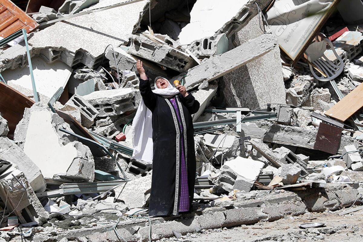 A woman surrounded by the wreckage of a building holds her arms up and cries.