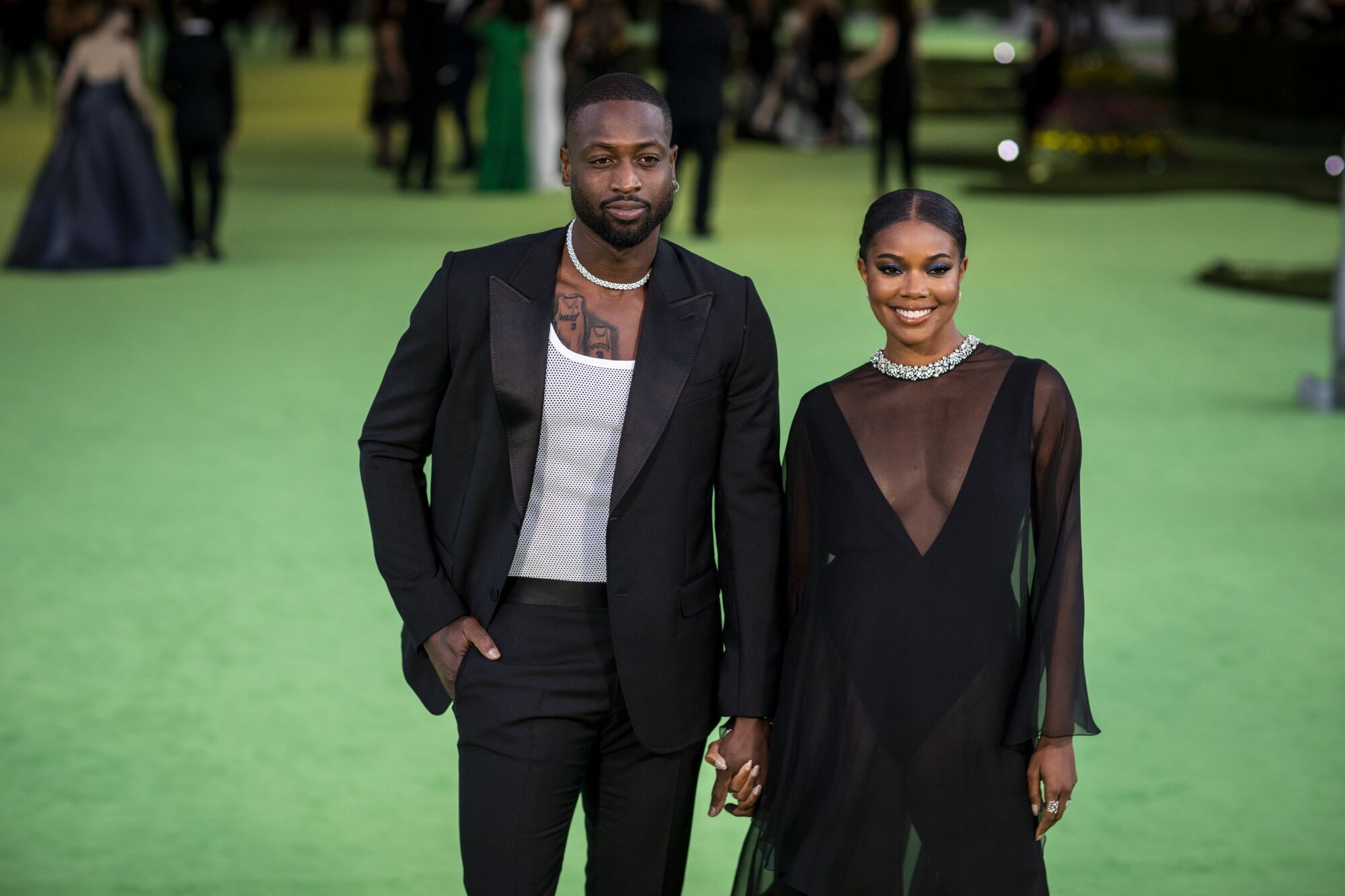 A man in a black suit and a woman in a black dress posing on a green carpet