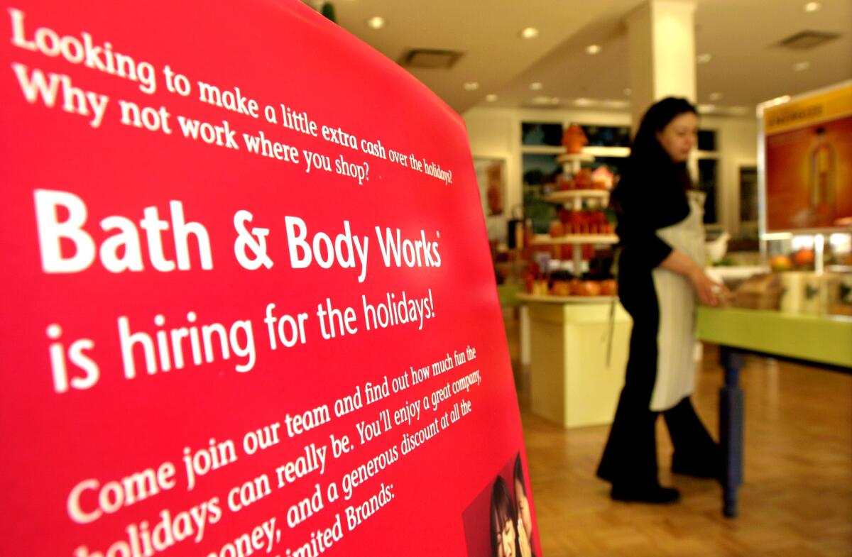 Red sign advertising holiday hiring at Bath and Body Works with a worker in the background.