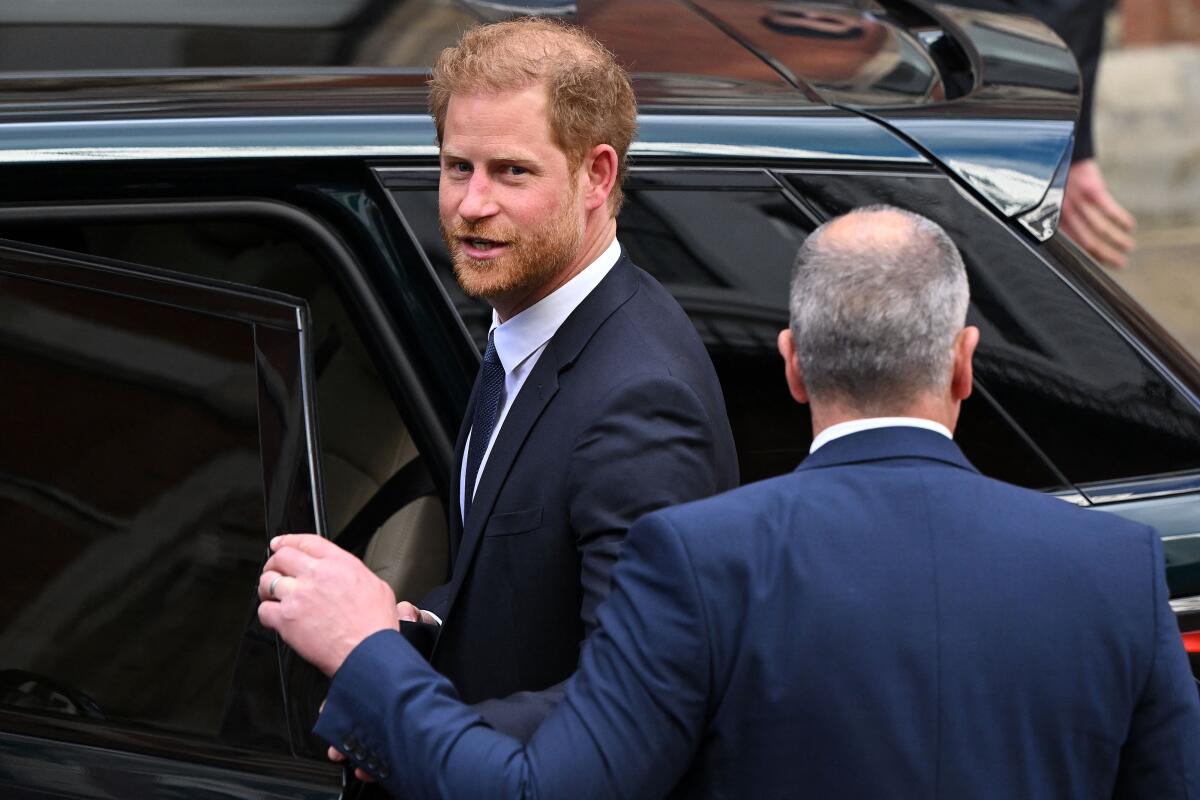 Prince Harry looks back toward the camera as he prepares to enter a car.
