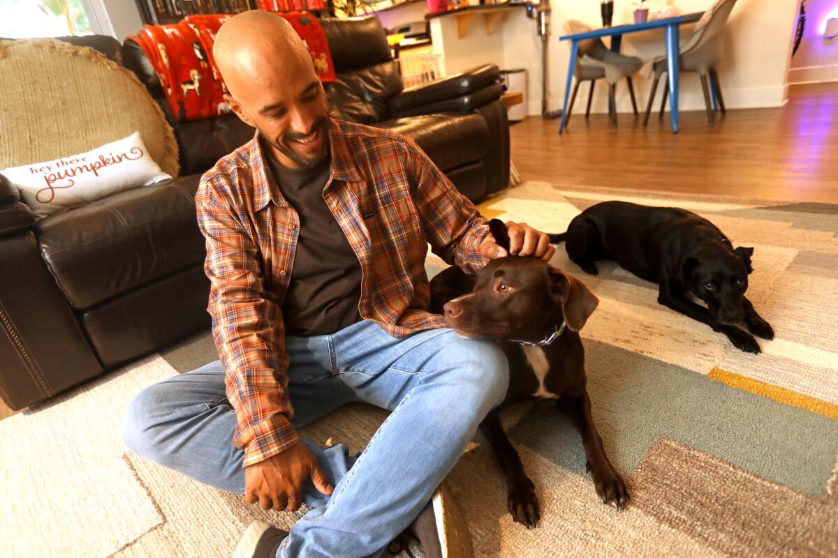 A man sits on a living room floor with two dogs