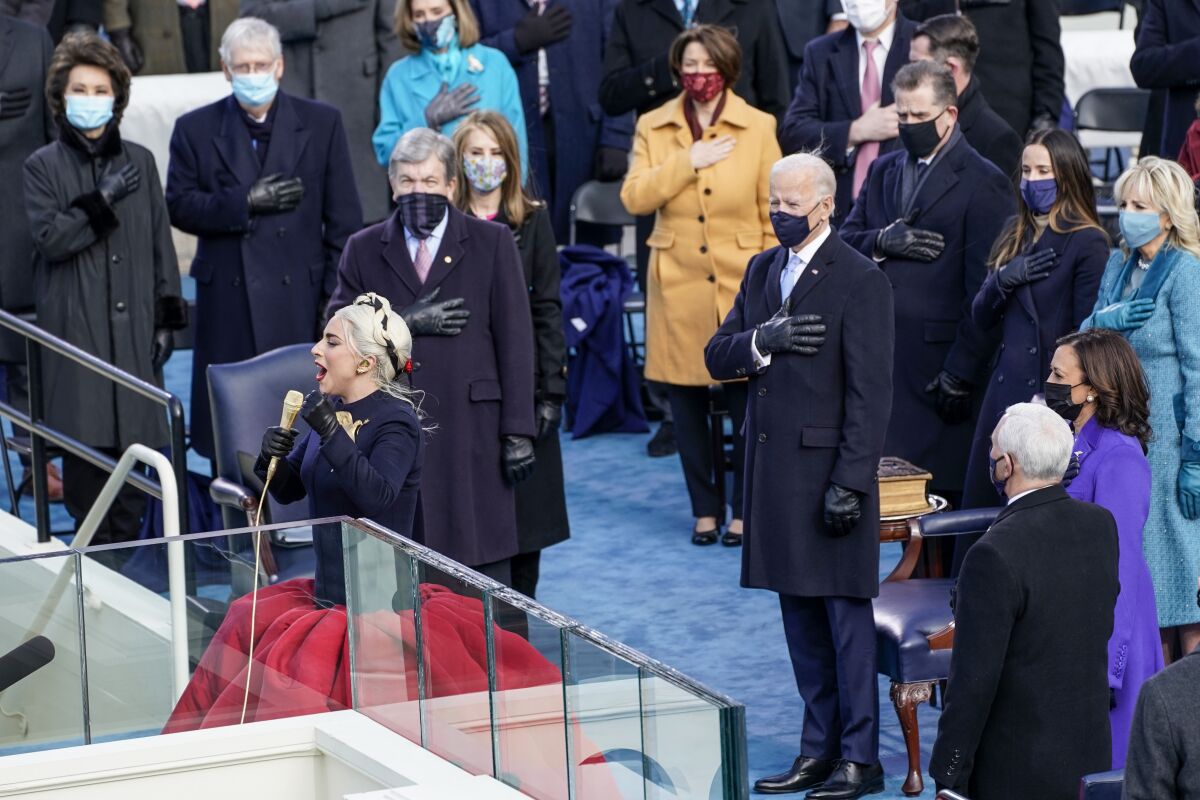 Lady Gaga performs the national anthem while people stand behind her, hand over heart.