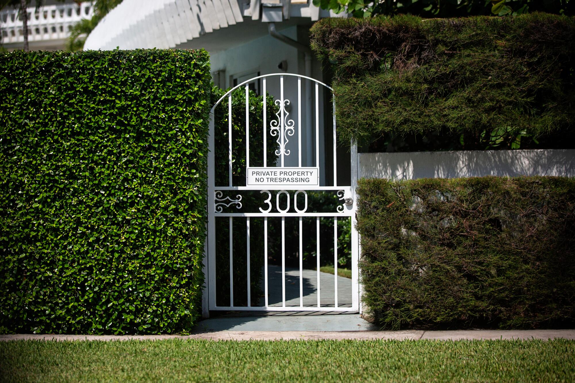A large hedge and a gate with a no-trespassing sign obscures the view of a large home in Palm Beach.