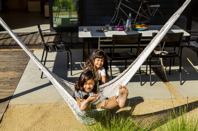 Two children play with a hammock on a patio.