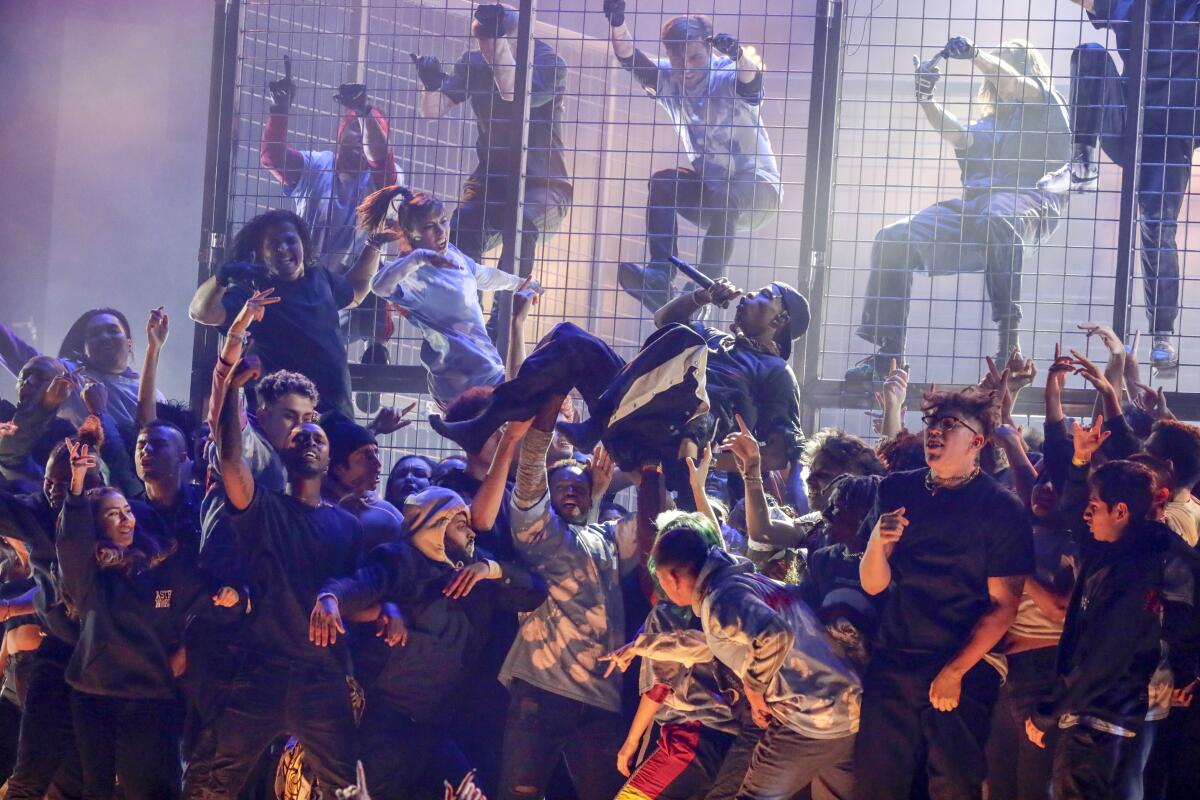 Travis Scott performs at the 61st Grammys surrounded by people, some in a cage behind him.