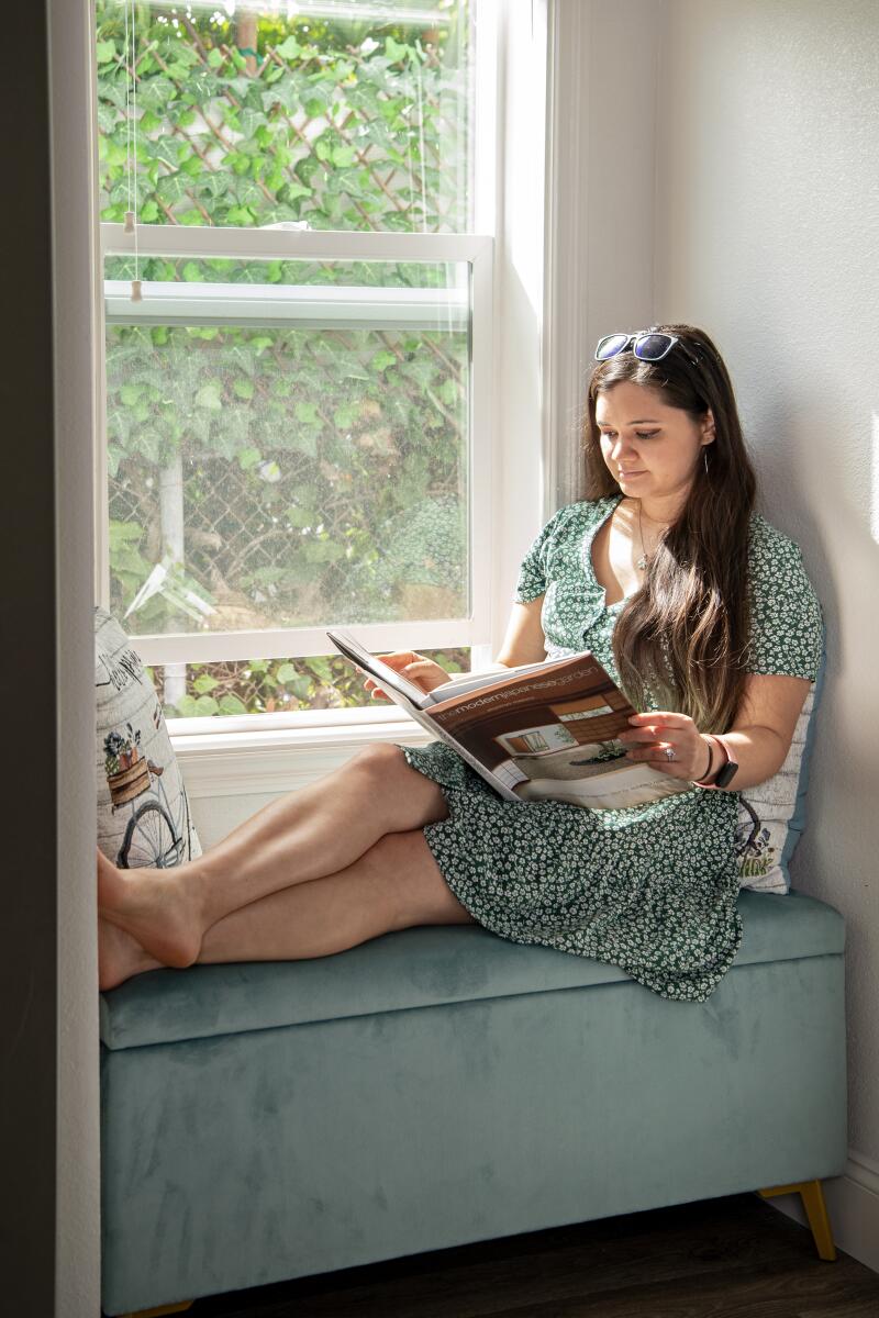 A woman sits in a window sill, reading a book.