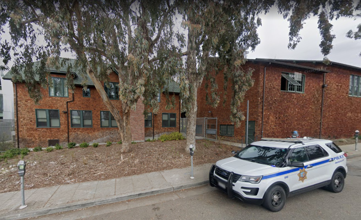 A police cruiser on the street outside a red brick building.