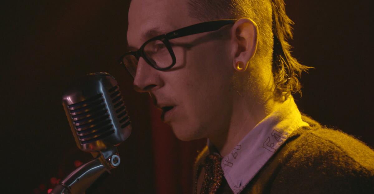 A man wearing glasses sings into a microphone.