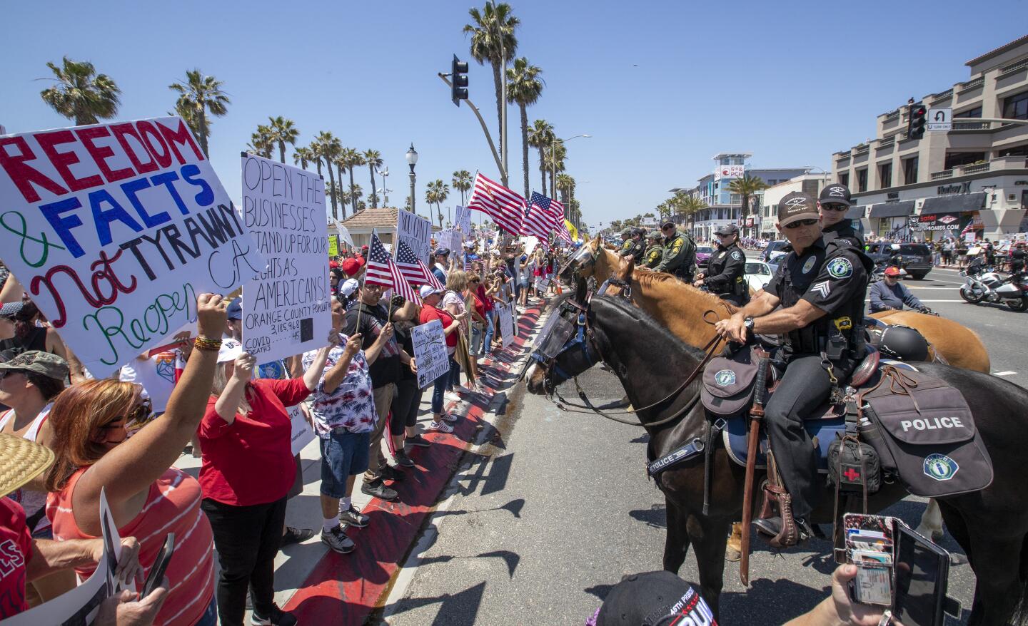 Police line up to keep protesters on the sidewalk in Huntington Beach