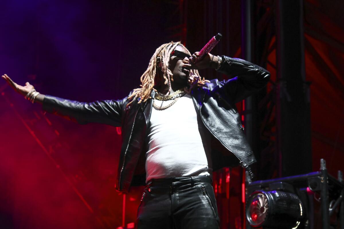Young Thug with blond braids standing onstage in a white shirt and a black leather jacket holding a mic to his mouth