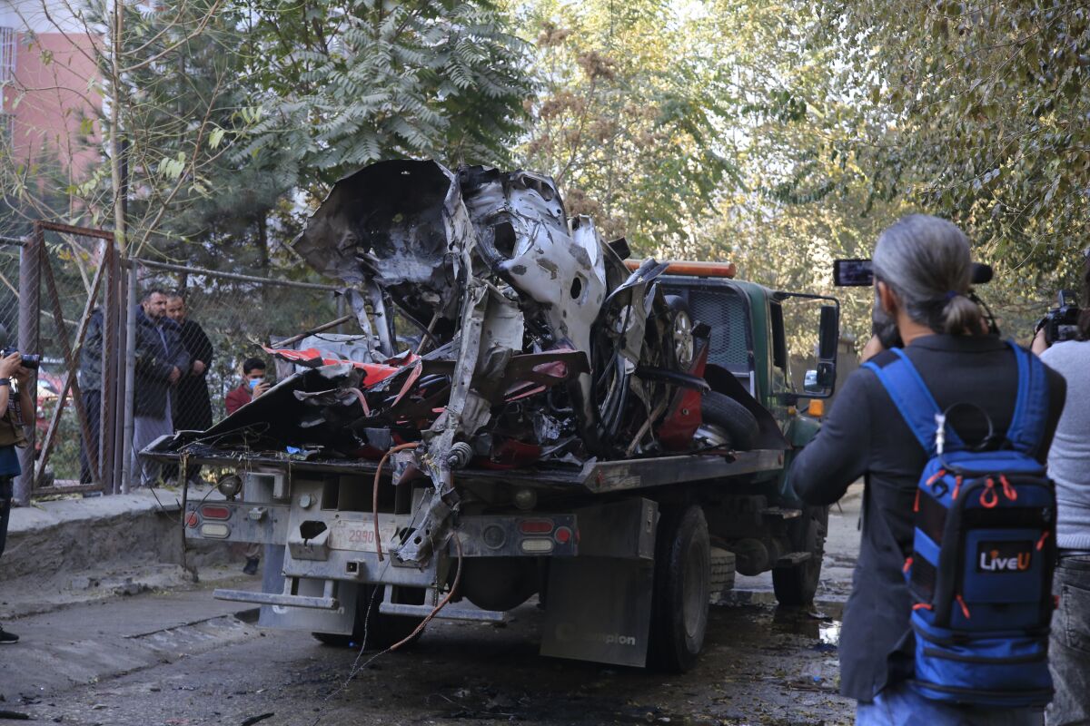 Afghans check a car destroyed by an attached bomb in Kabul