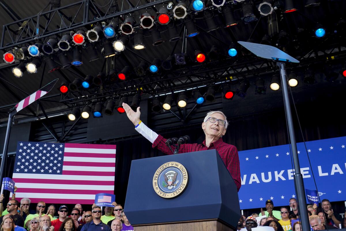 Wisconsin Gov. Tony Evers speaks at a rally with crowds and an American flag behind him. 