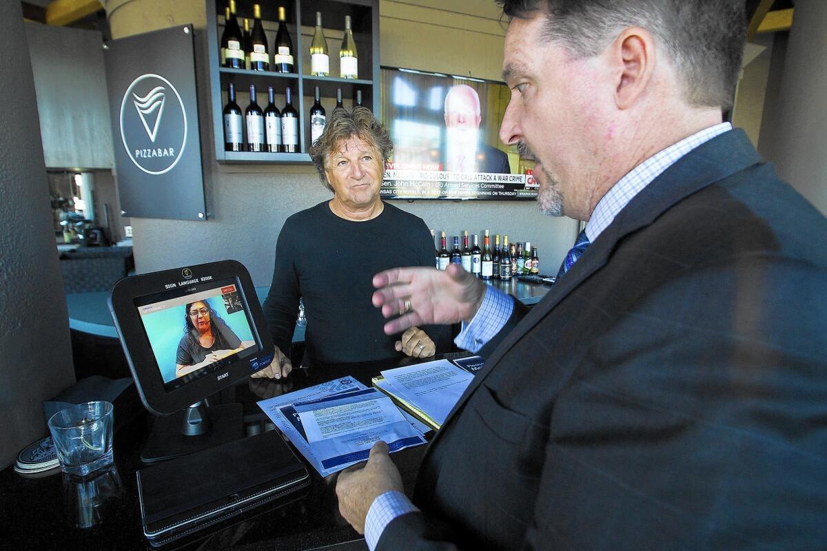 Tom Gruenbeck, right, an attorney for Language People, and Gary Decker, primary owner of PizzaBar in Newport Beach, demonstrate the restaurant's sign-language interpretation kiosk.