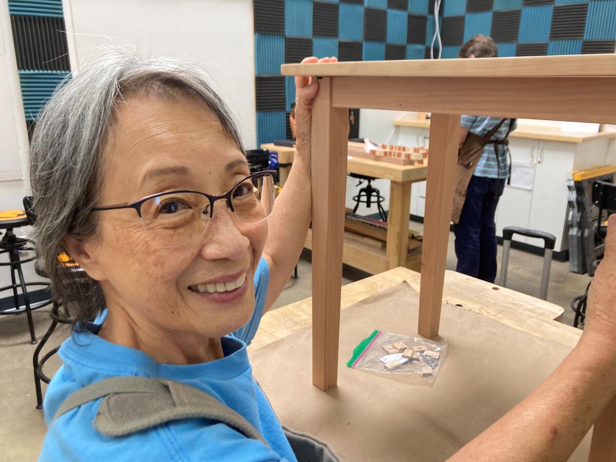 A woman shows off a table she is working on at a woodworking shop.