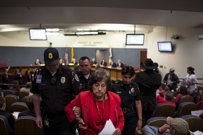 Police escort activist Nora Tachias-Anaya out of a city council meeting in Albuquerque, N.M.