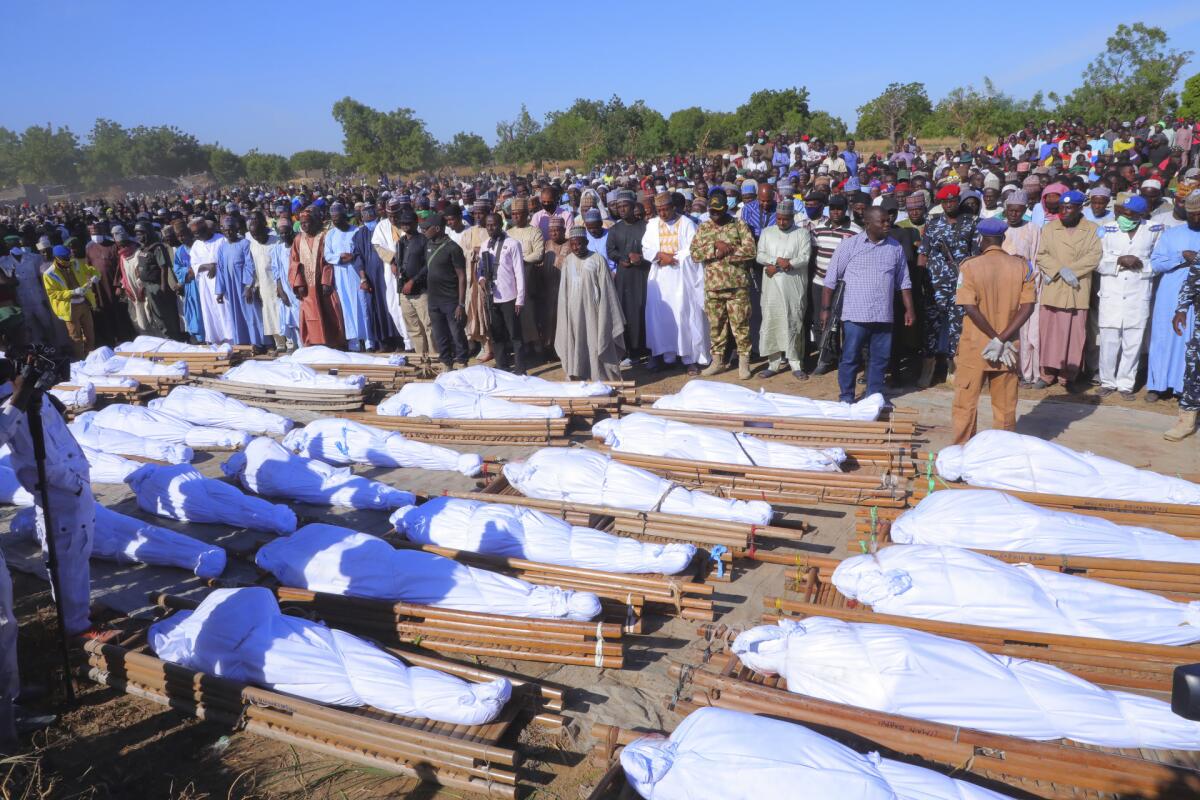 Many people attend a funeral for those killed. The bodies are wrapped in sheets and rest on pallets.