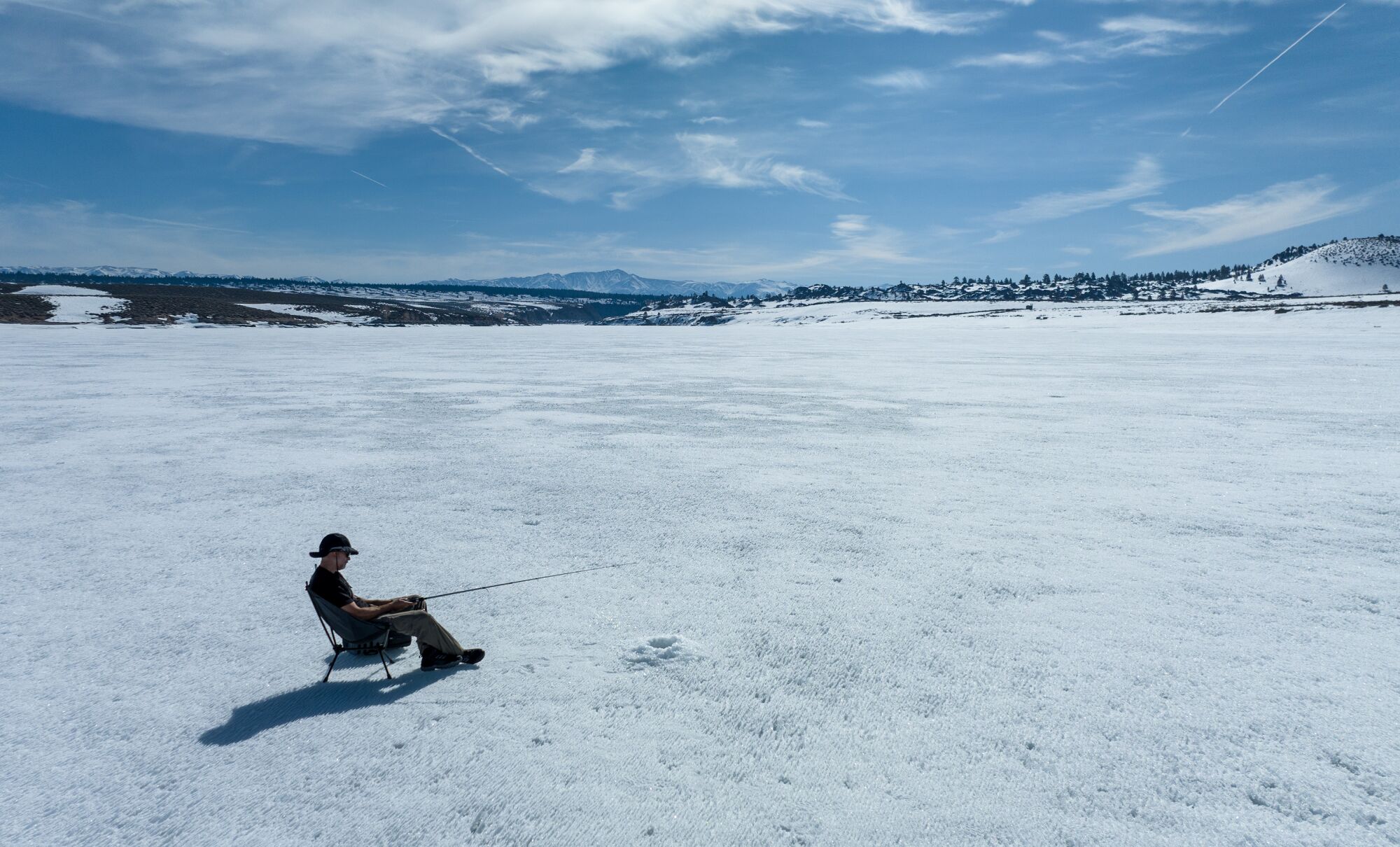 A fisherman sits next to a hole cut into frozen Crowley Lake.