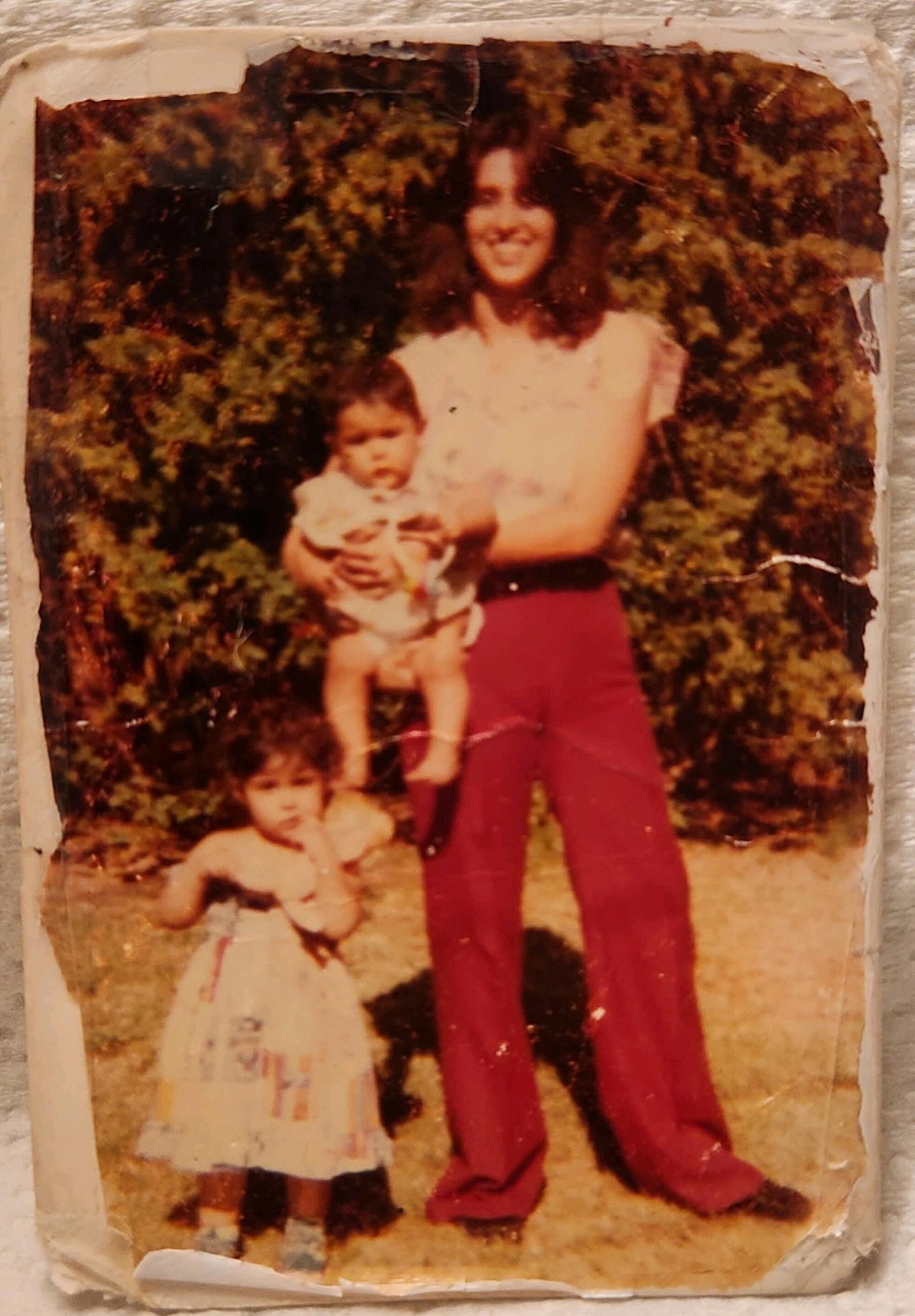 Photo of an old print image of Rachel Zendejas posing with a toddler standing by her leg and holding a baby.