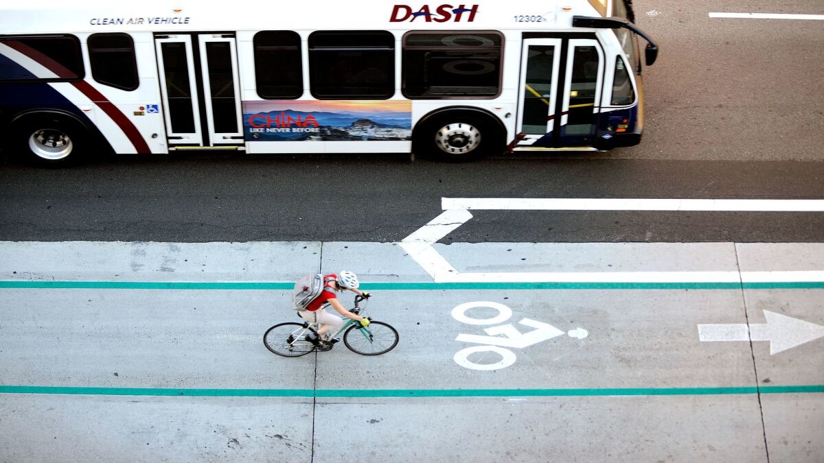 A DASH bush drives alongside a cyclist using a bike line in downtown Los Angeles.