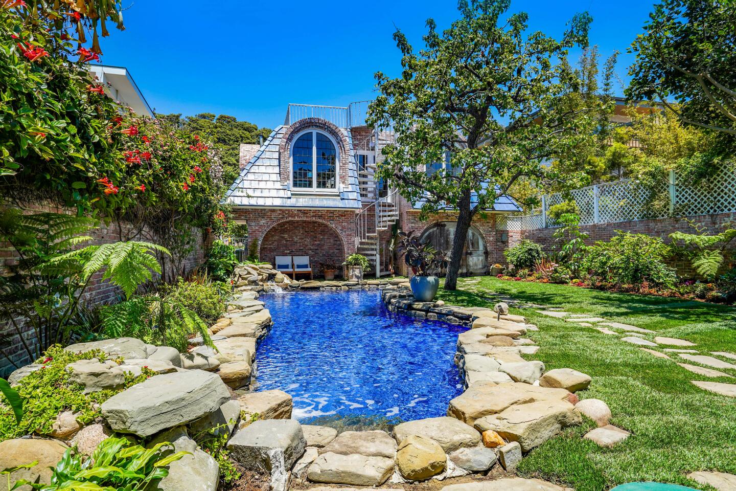 The brick beach house has landscaped grounds with a stone surrounded pool.