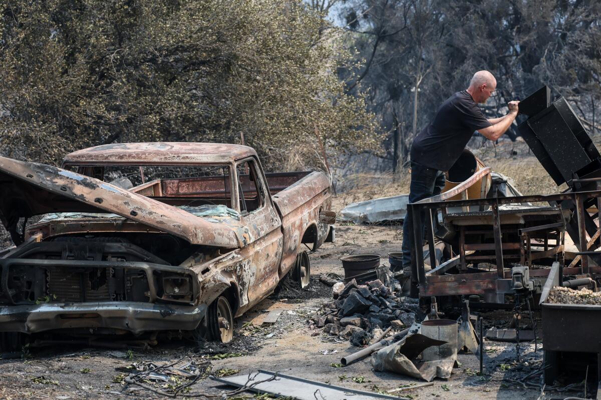 Sean Rains inspects his shake table next to the rubble of his home and a burned-out pickup truck.