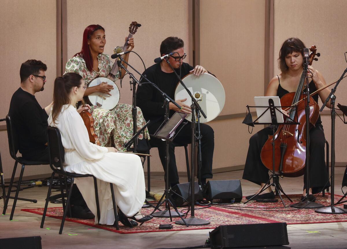 Five people play instruments, including a cello and banjo