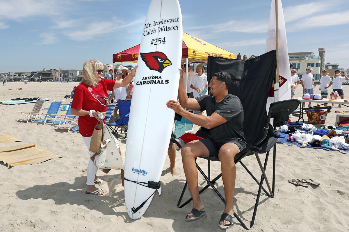 Irrelevant Week CEO Melanie Salata-Fitch, left, hands 2019 Mr. Irrelevant Caleb Wilson his honorary surfboard during the second day of the Irrelevant Week festivities in Newport Beach on June 29, 2019.