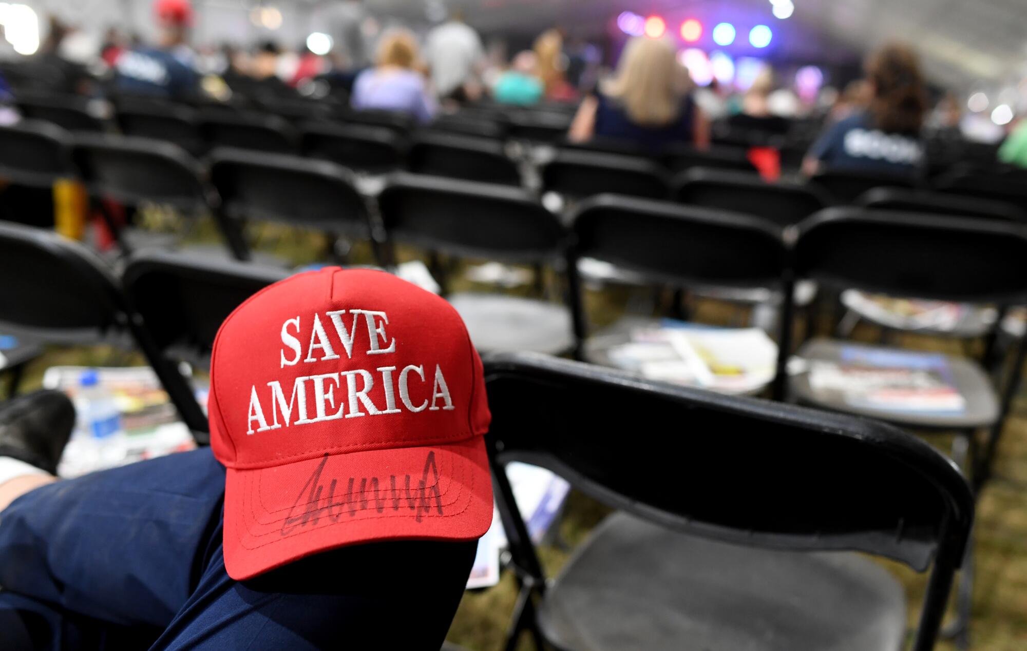 A person with a red cap that says "Save America" and an autograph on its bill 