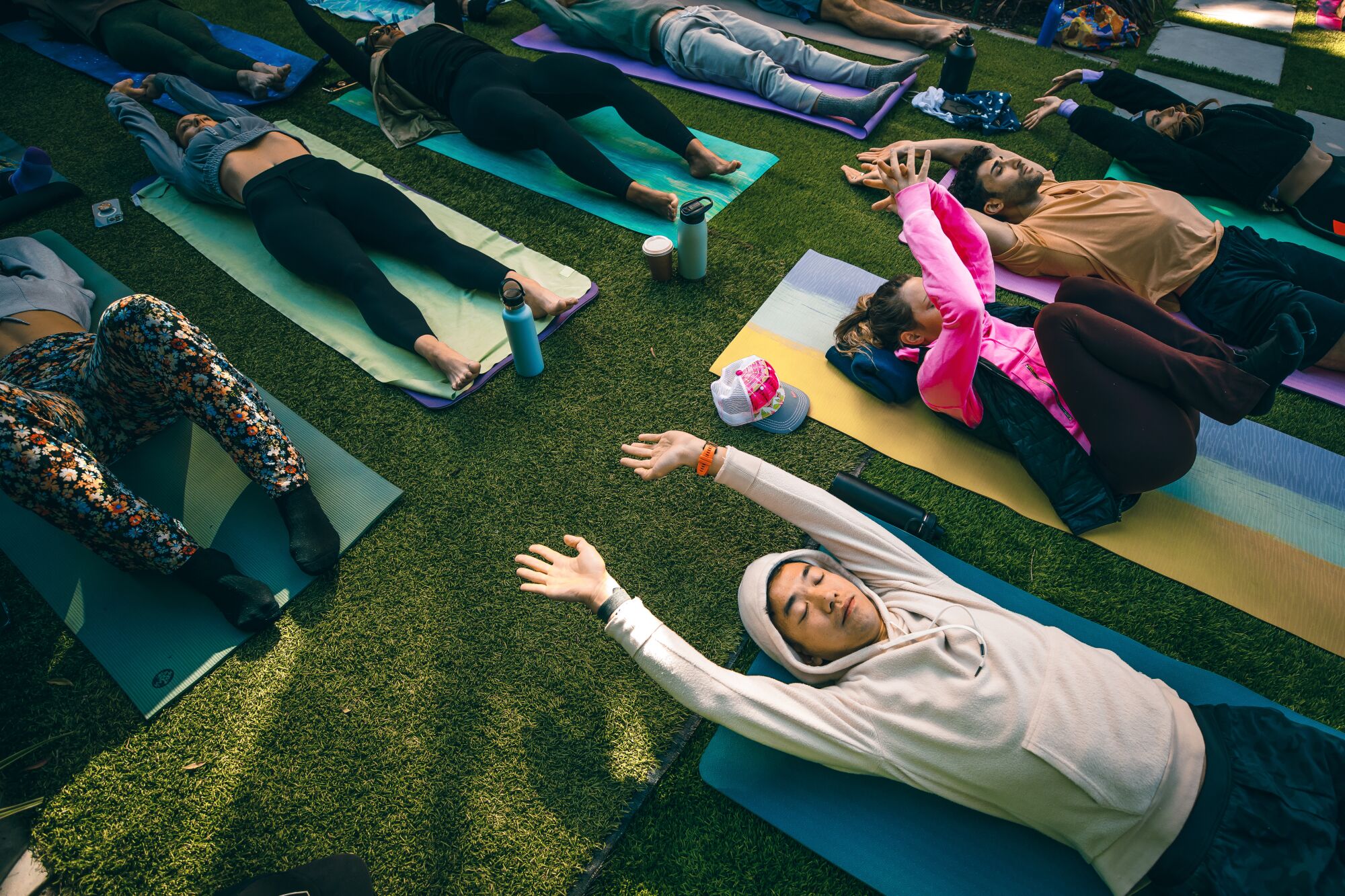 People lie on yoga mats outdoors, stretching