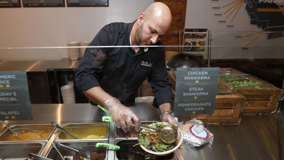 Hazem Karadsheh, SAJJ Mediterranean director of operations for Southern California, assembles a chicken curry salad bowl at the new SAJJ Mediterranean restaurant in Irvine.