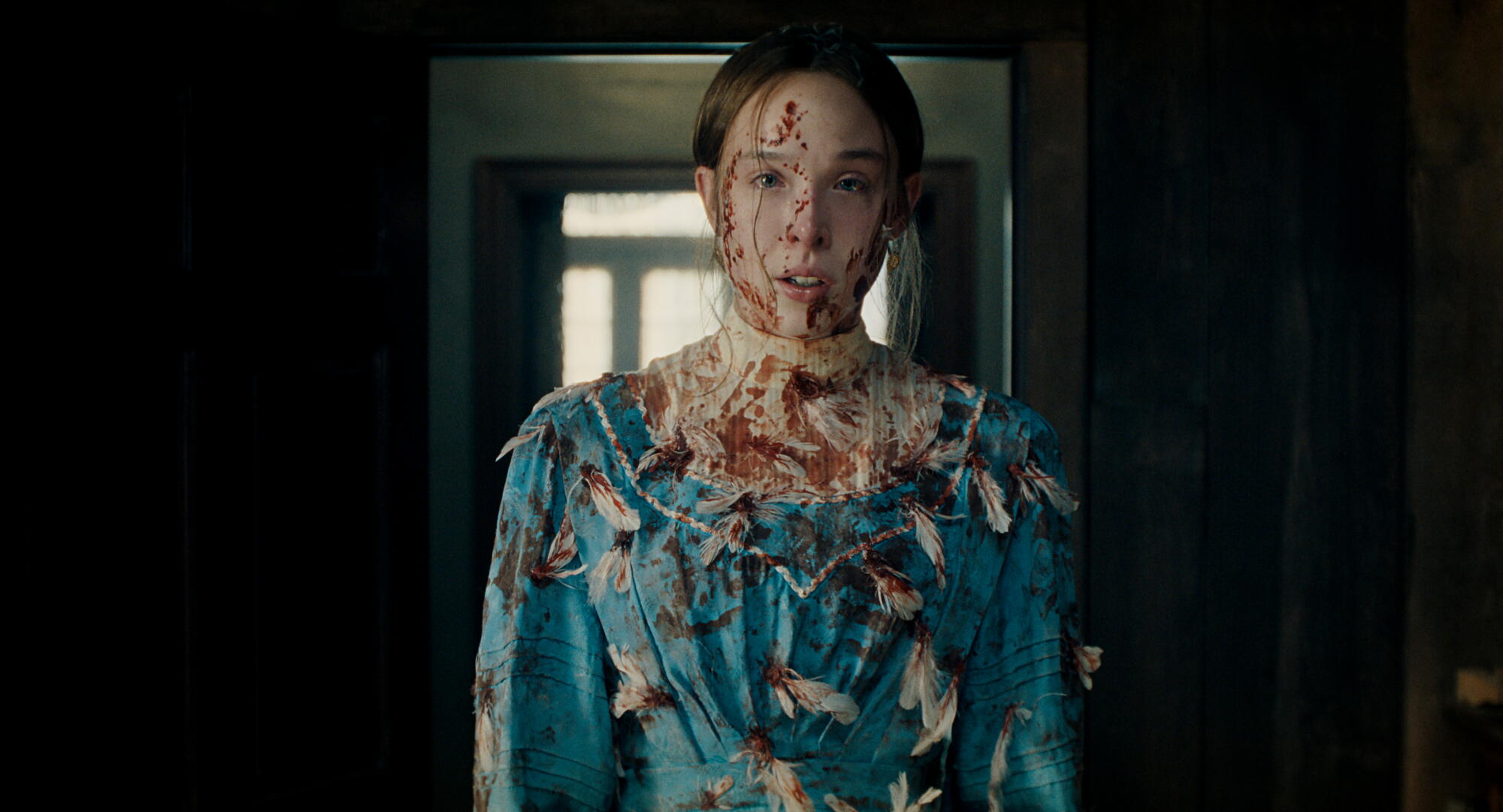 A woman in a blue dress covered in feathers and splatters of blood.