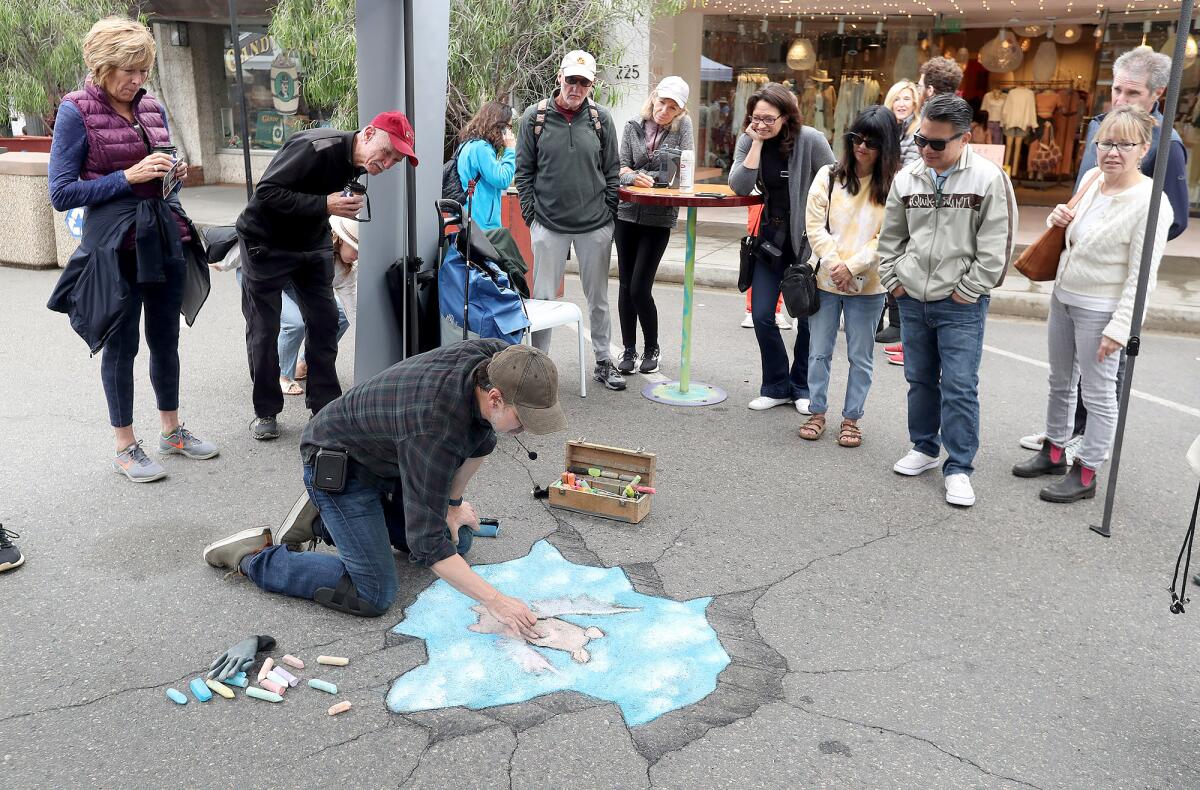 A crowd gathers around David Zinn, who draws a piglet with wings, during a public demonstration on the Promenade on Forest.