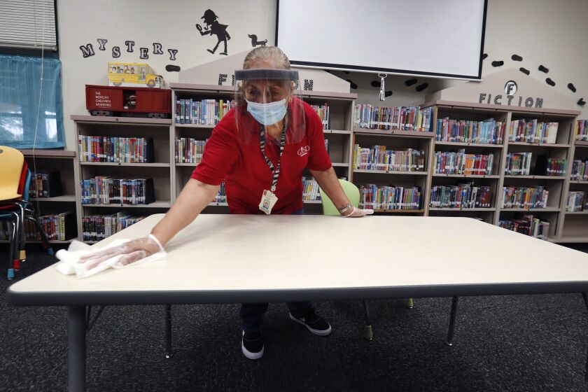 Wearing a mask and face guard as protection against the spread of COVID-19, Garland Independent School District custodian Camelia Tobon wipes down a table in the library at Stephens Elementary School in Rowlett, Texas, Wednesday, July 22, 2020.(AP Photo/LM Otero)