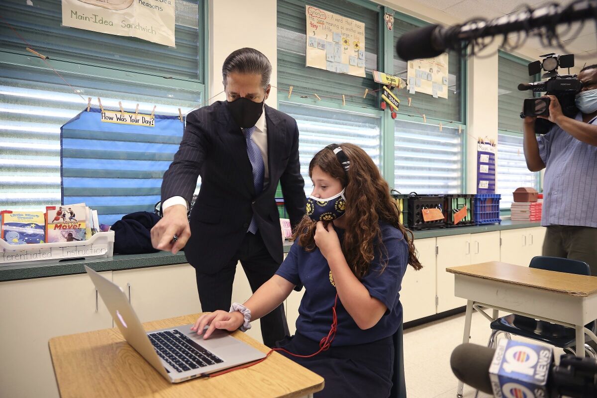 FILE- In this Aug. 31, 2020 file photo, Miami-Dade County Public Schools' superintendent Alberto Carvalho glances towards student Emily Acosta as she does school work in her mother's class as he stopped by Bob Graham Education Center in Miami Lakes, Fla. Authorities announced, Thursday, Sept. 3, 2020, that a 16-year-old student has been arrested for orchestrating a series of network outages and cyberattacks during the first week of school in Florida's largest district. (Carl Juste/Miami Herald via AP, File)
