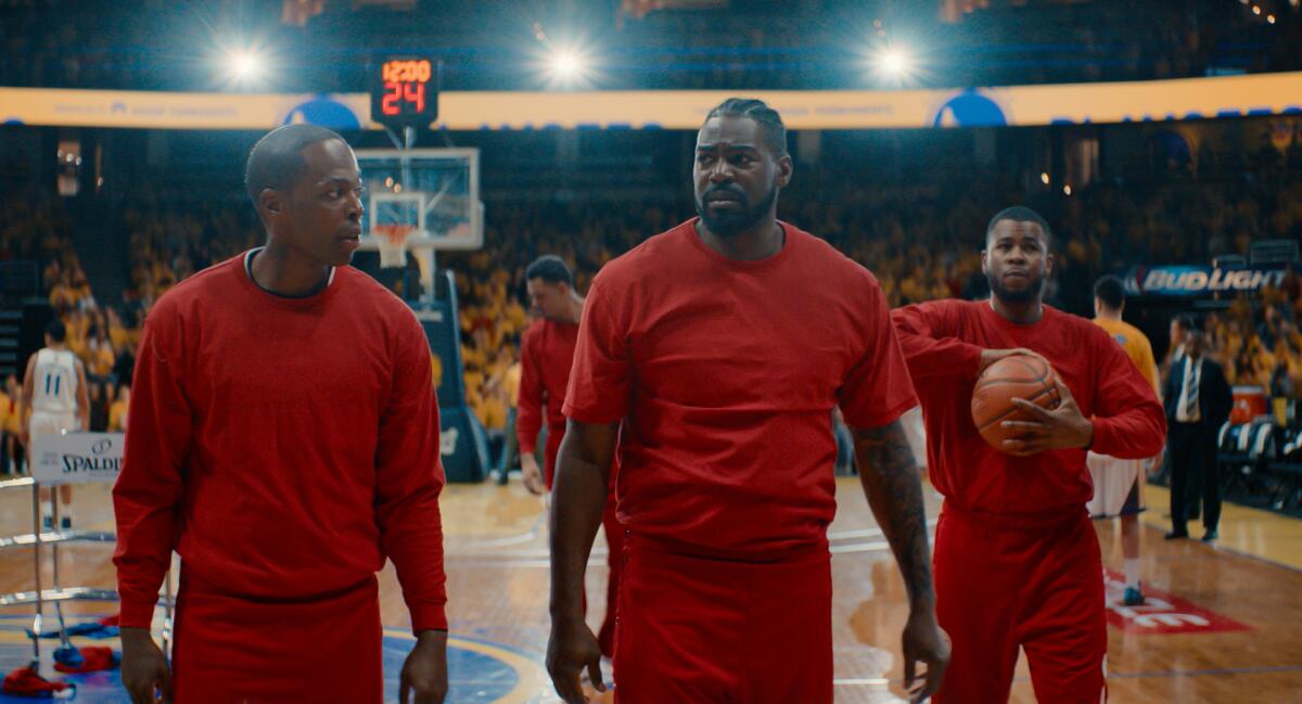 Three men in red sweats on a basketball court.