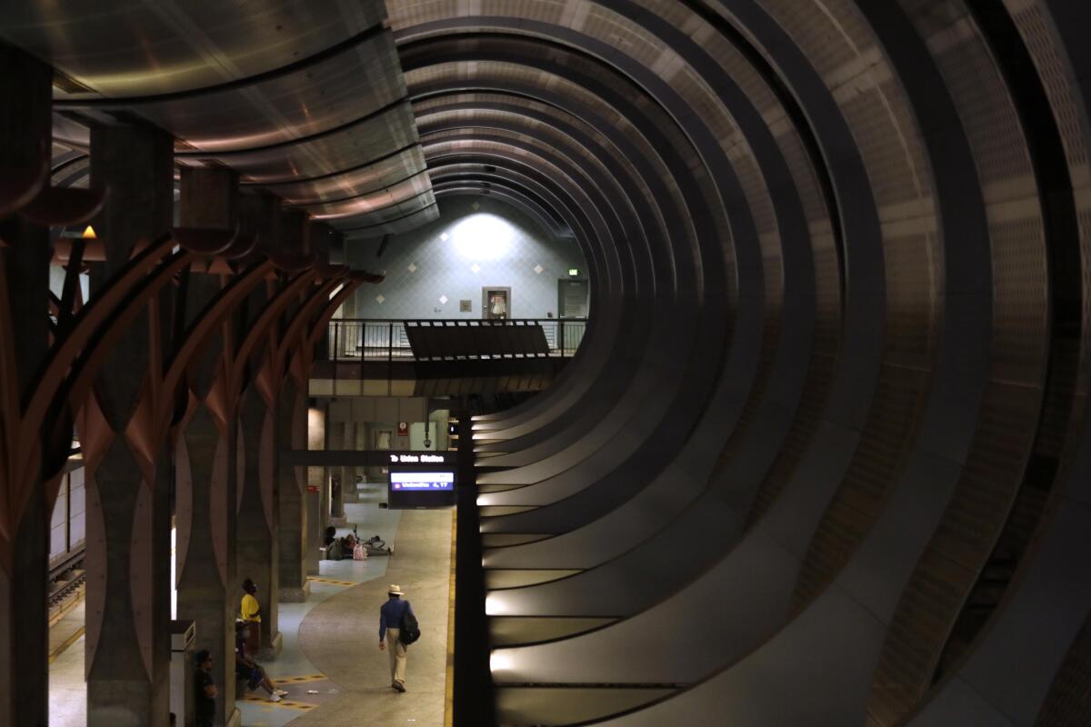 A commuter at a subway station makes their way along a platform underneath curving ceilings.