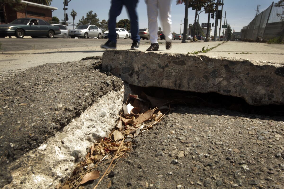 Two people navigate the cracked sidewalk along Vermont Avenue where it meets the 101 Freeway in Los Angeles.