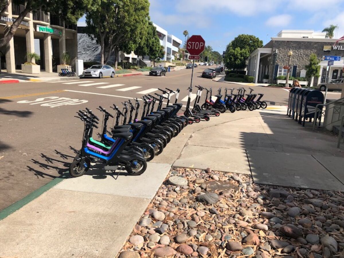 Electric bikes and scooters are stationed outside the Wall Street post office in La Jolla in violation of city staging rules.