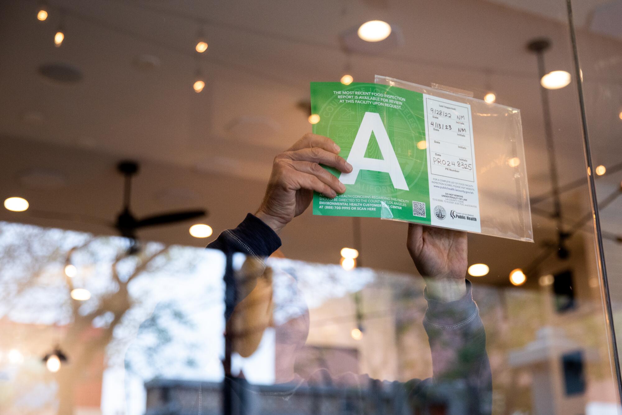 A person posting an A graded health inspection sheet on a window.