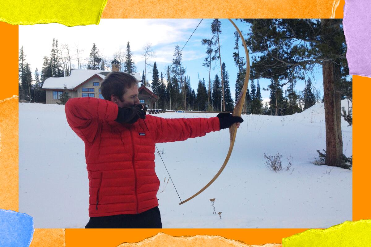 Surrounded by a snowy scene with tall trees, Eric Clem pulls back on his wooden bow.