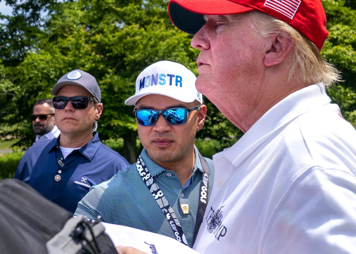 Walt Nauta, center, and Donald Trump at right in profile. A third man is at left. All wearing caps 