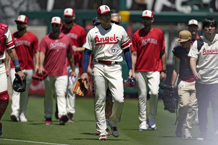 The Angels' Shohei Ohtani is surrounding by teammates as he walks from the bullpen onto the field before a game