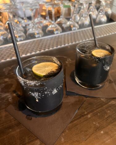 Two glasses with a black cocktail garnished with citrus slices