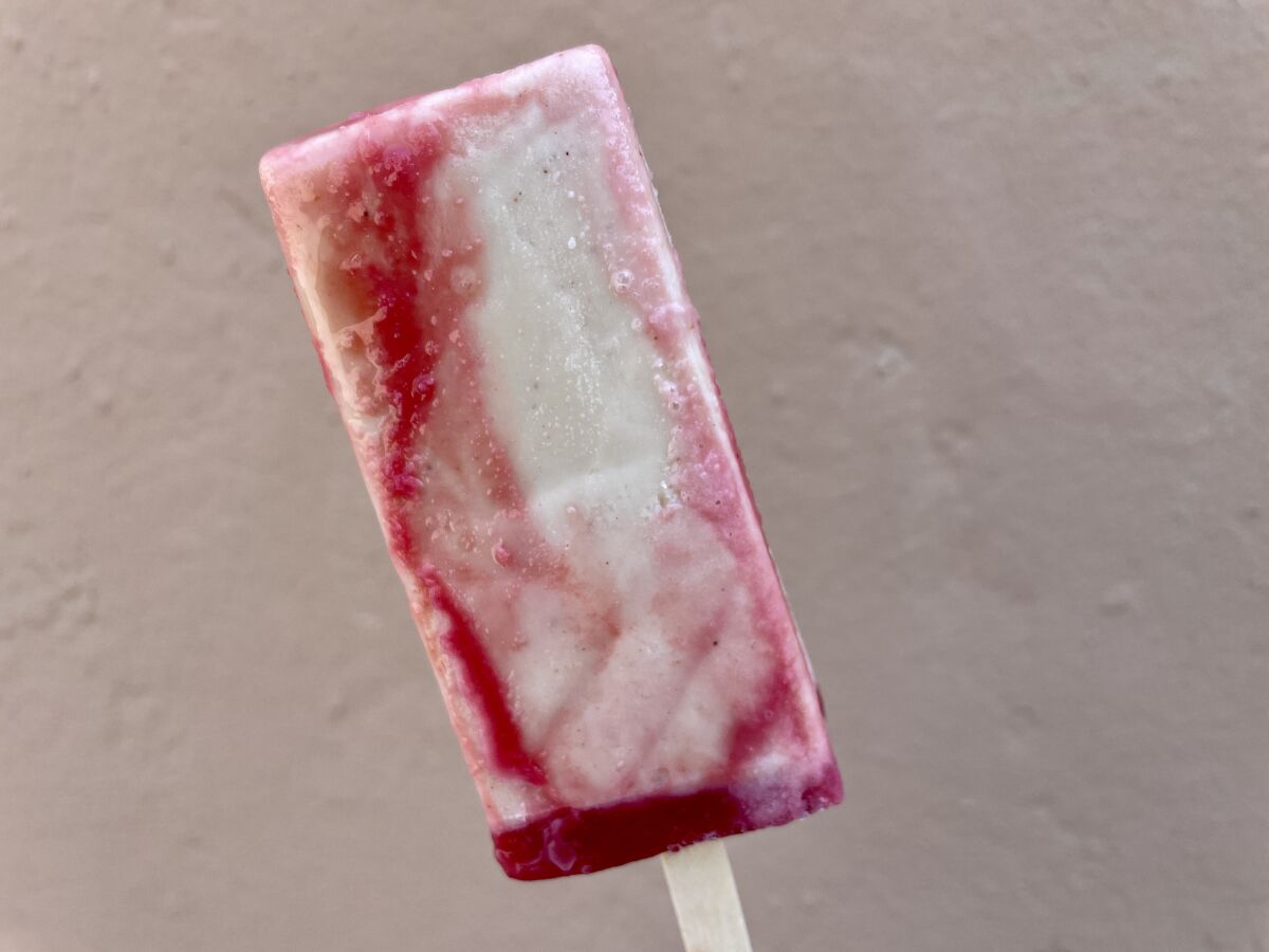 A red and white frozen treat on a stick.