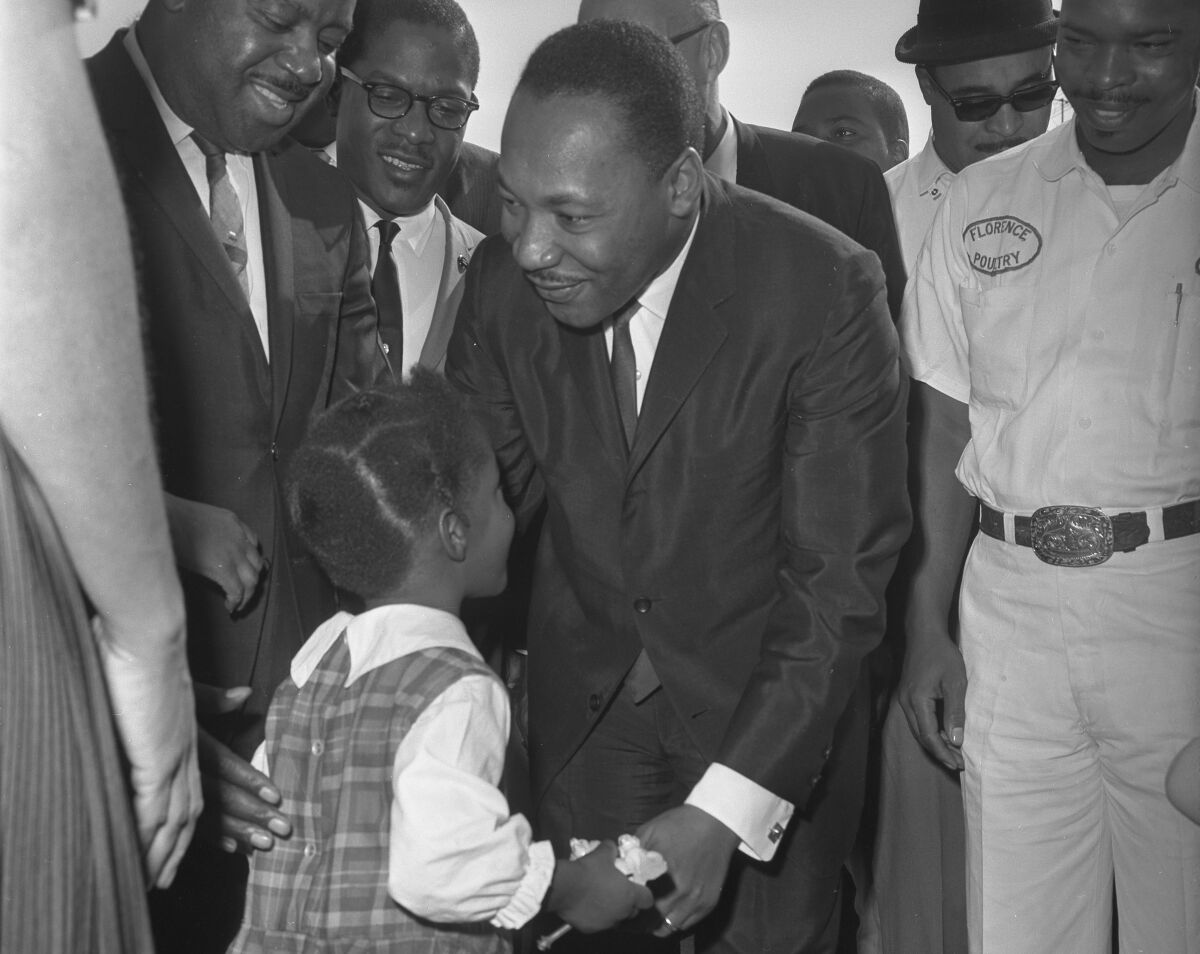 Dr. Martin Luther King Jr. smiles and bends toward a small girl in a plaid dress.